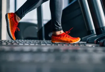 A person wearing gray exercise pants and orange and red shoes walks on a treadmill.