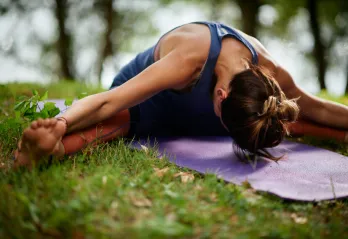 A woman does a yoga stretch outside.