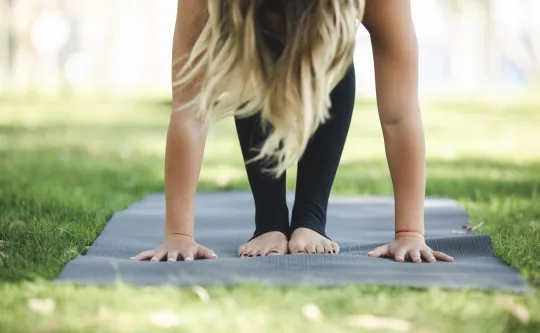 A woman stands on a mat while doing yoga outdoors.