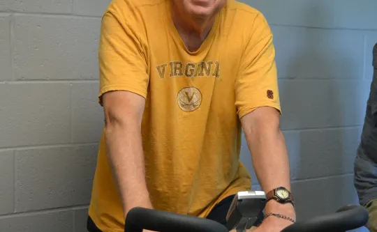 A man smiling at the camera while sitting on a stationary bike.