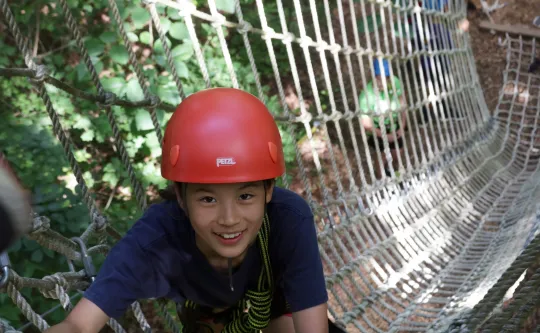 A camper at YMCA Camp Weaver smiles into the camera while climbing a ropes course.