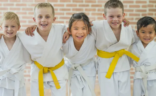 A diverse group of children smiling at the camera. They are dressed for a tae kwon do class.