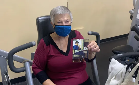 Ms. Hilda is sitting on a chair showing his before picture.