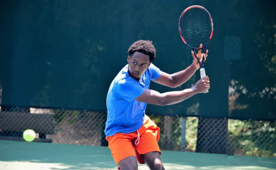 A man playing tennis outdoors prepares to hit an oncoming tennis ball.