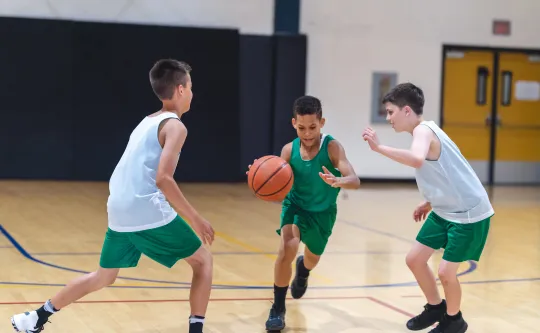 Three young boys playing basketball in a gym.