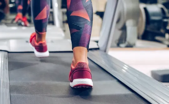 A woman wearing exercise clothing walks on a treadmill.