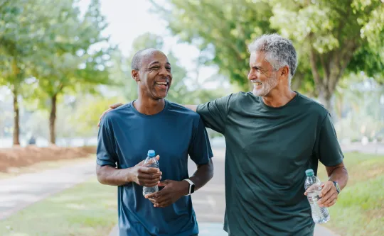 Two senior friends walking outside together. Both men are laughing.