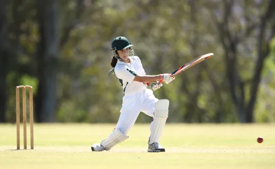 A young girl batting while playing cricket.