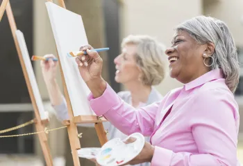 A senior woman smiling while painting during a class.