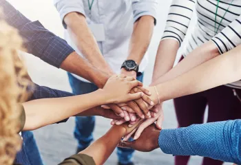 A diverse group of people standing in a circle with their hands stacked in the center.