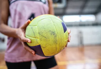 A close-up of a woman holding a yellow and purple volleyball.