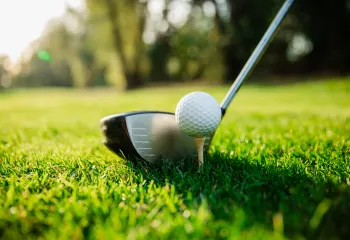 A close-up image of a golf ball on a tee. A golf club is poised near it.