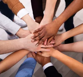 A diverse group of people standing with their hands in a circle.