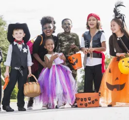 A diverse group of children in Halloween costumes standing outside.