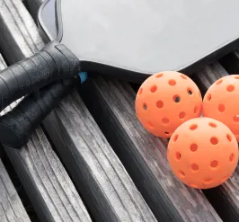 A pickleball raquet and pickleballs on a gray wooden background.