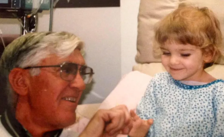 A little girl in the hospital smiles with her grandfather.