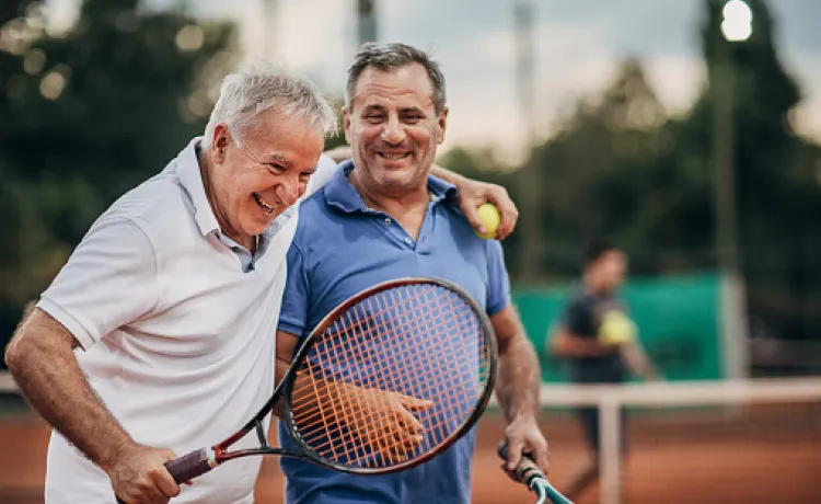 Two older adults laughing and bonding during tennis match.