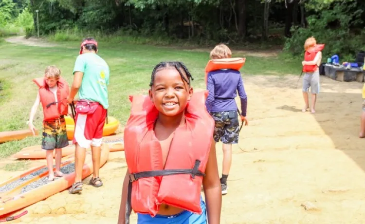 Kid with an orange lifejacket at summer camp.