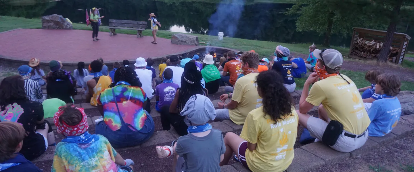 A group of campers at YMCA Camp Weaver sitting together at an ampitheater near a lake.