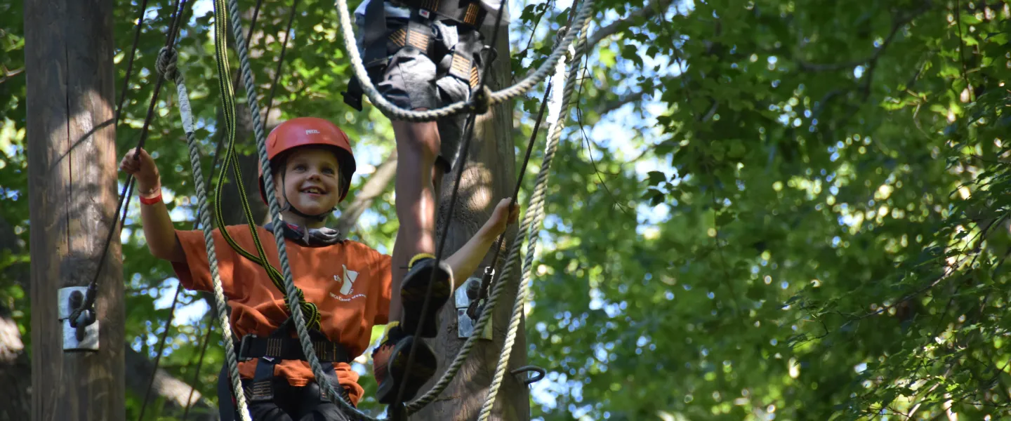 A boy smiles as he climbs on a ropes course.