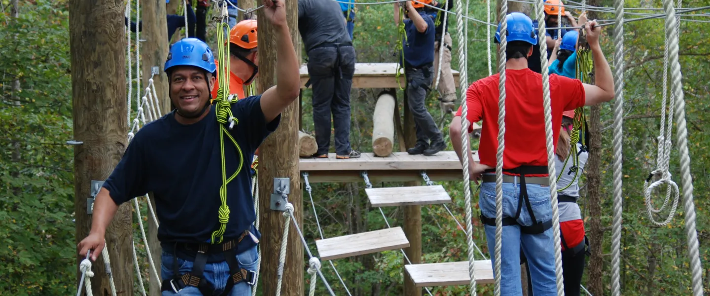 A group of adults at YMCA Camp Weaver walk across a ropes course.