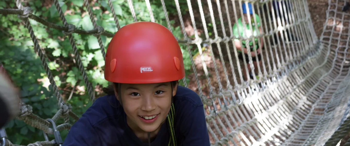 A camper at YMCA Camp Weaver smiles into the camera while climbing a ropes course.