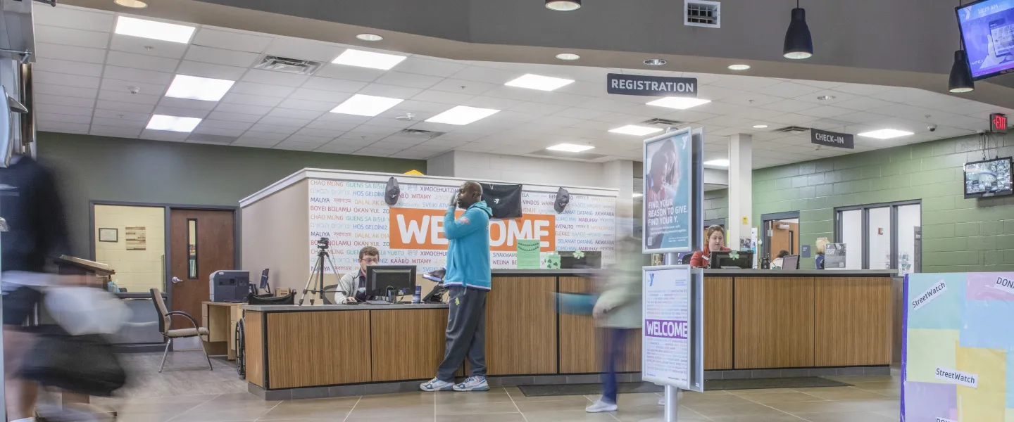 A photo of the Spears YMCA lobby and front desk. Members are seen exiting the building and standing near the font desk.