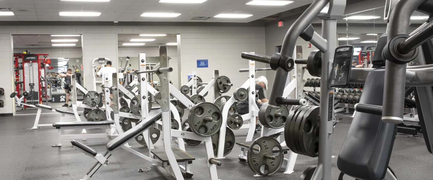 A photo of the weight room at the Spears YMCA. Black and white exercise machines are spread out along the black floor.