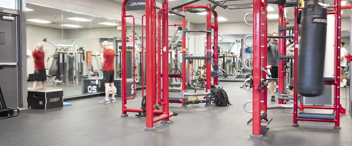 A photo of a weight room at the Spears YMCA. There is a punching bag hanging next to red exercise equipment used for various exercises.