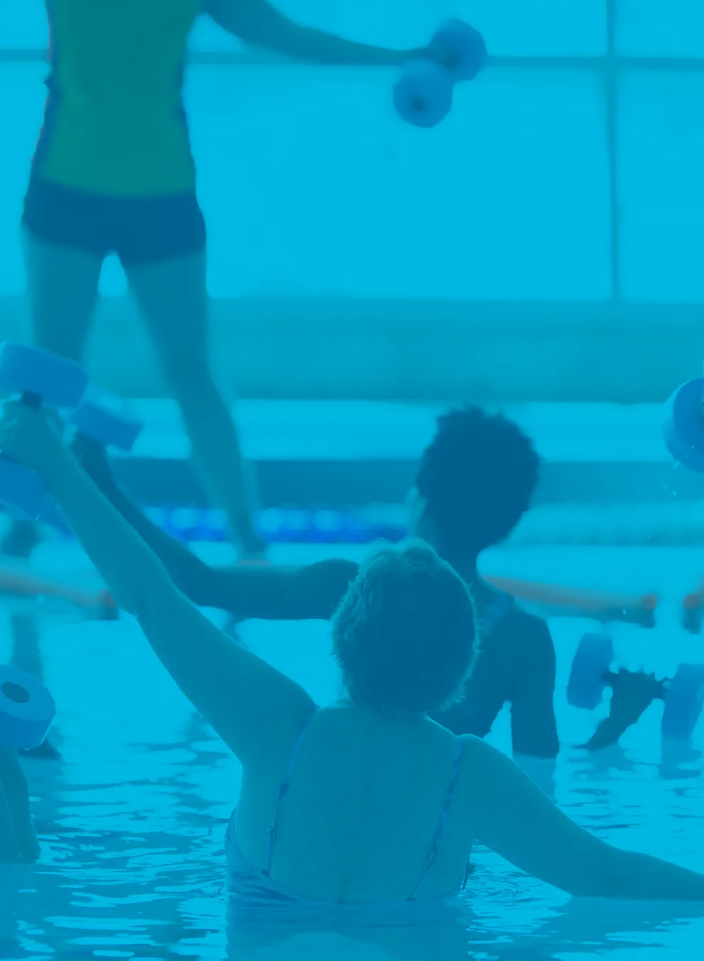 A group of women in a water fitness class. They are exercising with weights and their backs are to the camera while the instructor speaks to them.