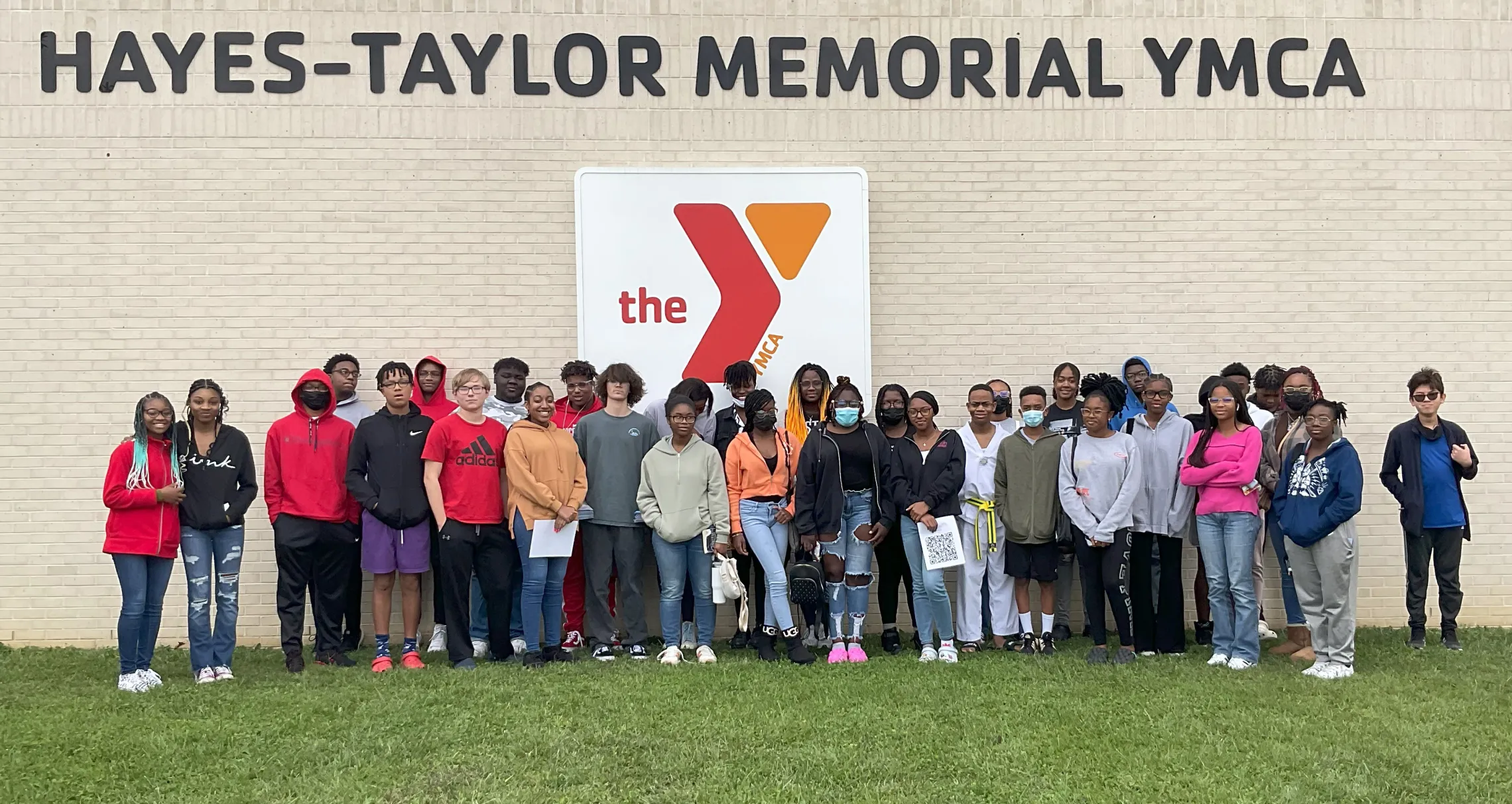A group photo of the YMCA of Greensboro Achievers. They are standing in front of the Hayes-Taylor YMCA's sign.