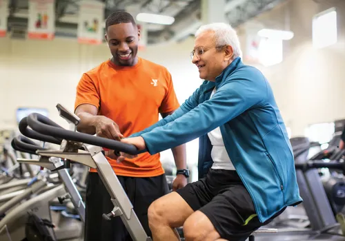 YMCA of Greensboro staff helping adult with gym equipment