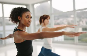 Two women in a yoga class holding a yoga pose and concentrating.