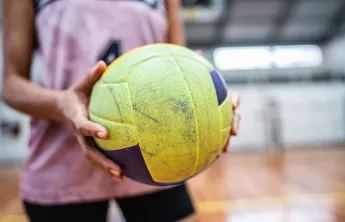 A close-up of a woman holding a yellow and purple volleyball.