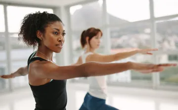 Two women in a yoga class holding a yoga pose and concentrating.