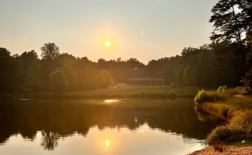 A view overlooking YMCA Camp Weaver's lake. There is a sunset in the background. The sun is warm and yellow and reflected in the lake. In the foreground is a path.