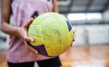 A close-up of a woman holding a yellow and purple volleyball.